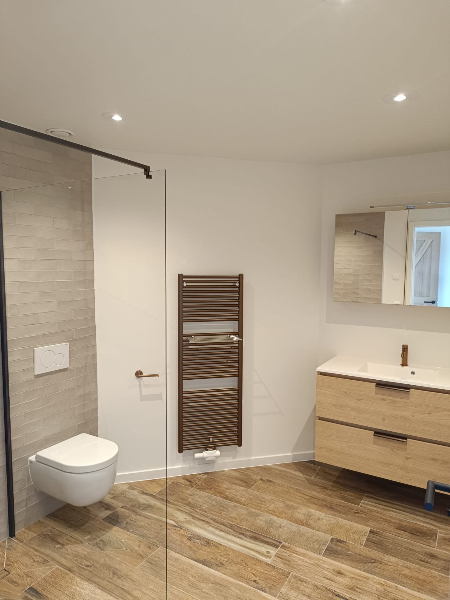 Moderne badkamer met houtlook vloer en glazen douchewand